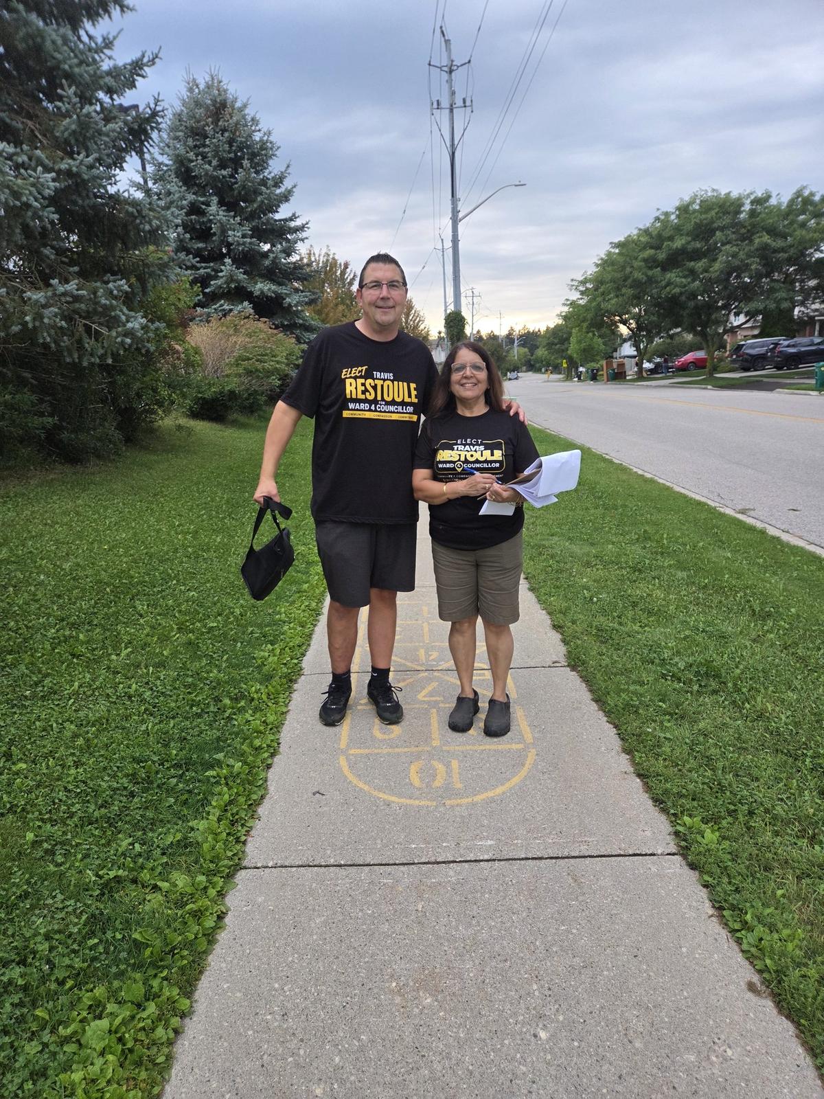 Travis Restoule and a campaign volunteer standing on a Ward 4 sidewalk at dusk after an evening of door knocking
