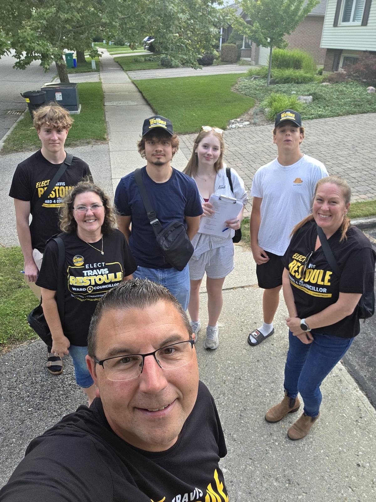 Travis Restoule taking a selfie with his volunteer canvass team on a Ward 4 driveway, clipboards in hand