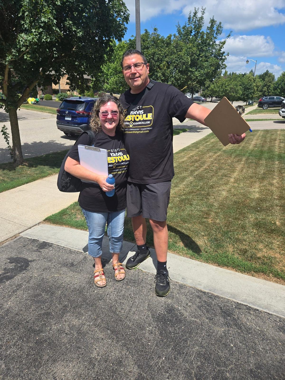 Travis Restoule and a volunteer holding clipboards while canvassing a sunny Ward 4 street